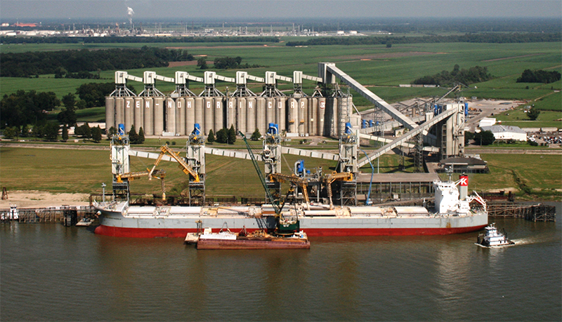 photo of a CGB Grain port that has a red cargo ship waiting to be loaded and behind it are bronze colored grain silos which keep the grain stored.